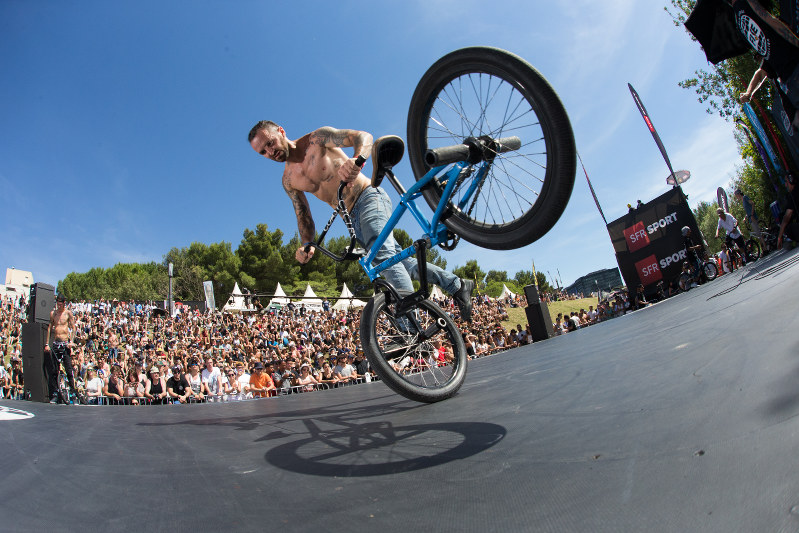 草むらに座る観客の前で、技を披露するBMXフリースタイルの選手。今年創設20年を迎えたFISEの今季のシリーズ初戦。スポーツクライミングなど多様な競技が同時に行われる=2017年5月、フランス南部モンペリエでFISE提供