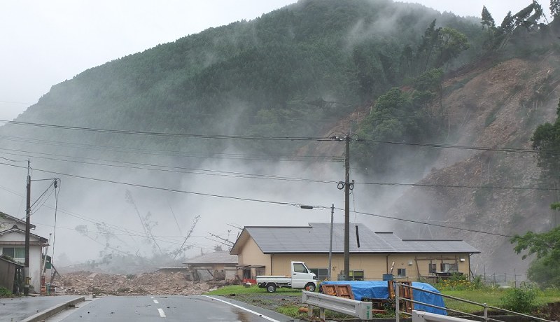 大分県日田市の小野地区で土砂崩れが発生した瞬間の様子。右側の山が崩落し、土砂は土煙を上げ、樹木をなぎ倒しながら県道に流れ込んだ=6日午前10時32分(住民提供)