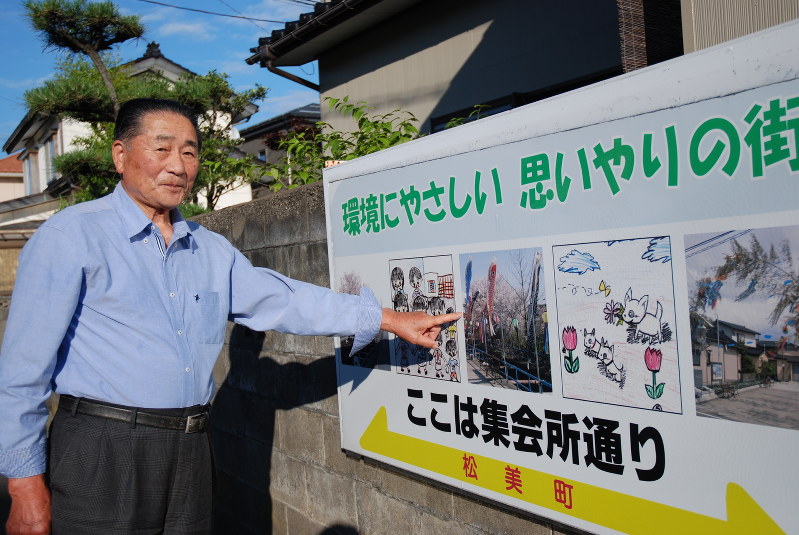 住民がつけた通りの名前が一目で分かる看板について説明する関矢登さん=柏崎市松美で