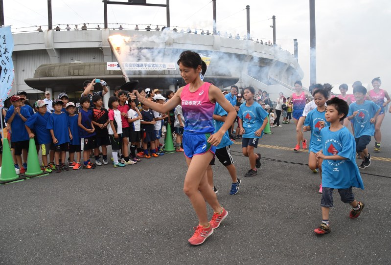 聖火台へ向け走る石巻専修大女子競走部主将の牧野あやさんと一緒に走る子どもたち=石巻市南境の市総合運動公園で