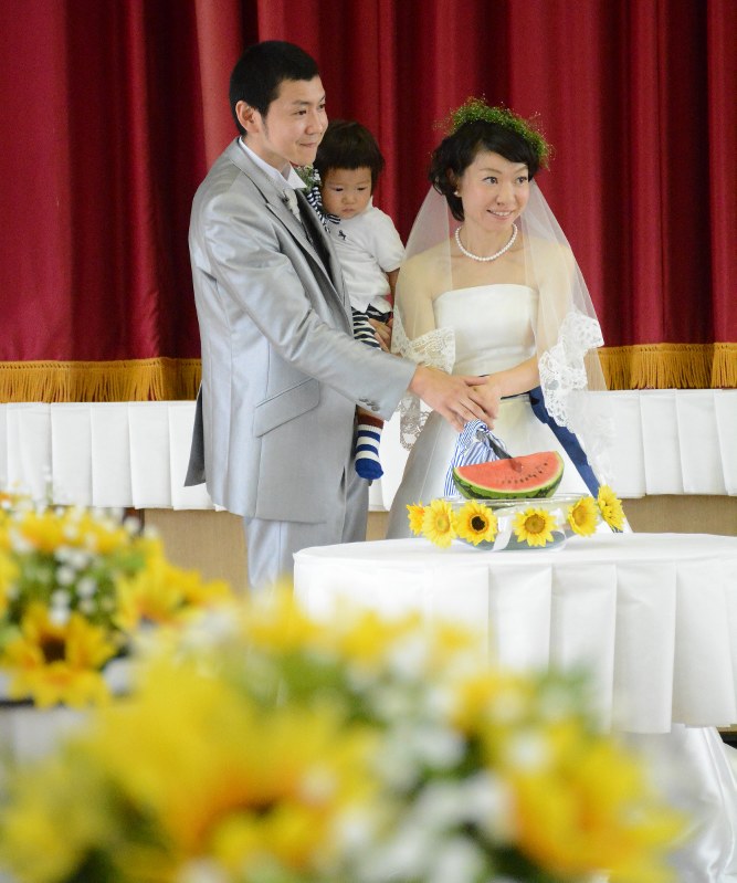 ひまわりの鉢植えに囲まれた会場でスイカに入刀する新郎新婦=津南町三箇甲の旧三箇小で