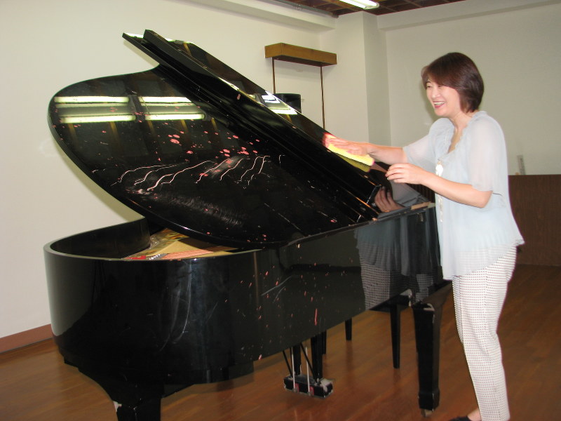 東日本大震災で津波をかぶりながらも修復されたグランドピアノを磨く鈴木由美さん。屋根や側板には大きな傷痕が残る=宮城県七ケ浜町の中央公民館で