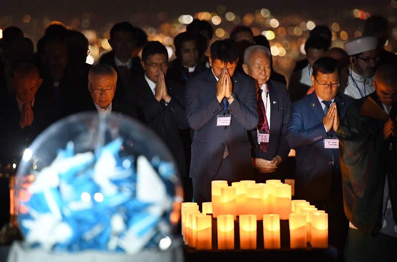球体に折り鶴を入れたオブジェ(手前左)を囲み黙とうする国内外の宗教者たち。奥は京都市街地=京都市山科区で2017年8月3日午後8時15分、大西岳彦撮影