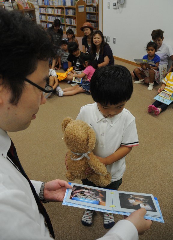 ぬいぐるみを受け取り、写真を見る男の子=江戸川区の篠崎子ども図書館で