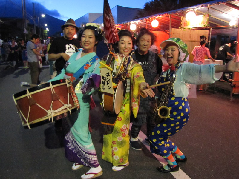 夏まつりのステージショーを終えて、夜店が並ぶ通りへ。中央のチンドン太鼓が好井ゆみこさん=八丈町で