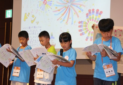 自分の描いた絵が背景に映し出されたステージで、作品を読む子どもたち＝韓国・済州島で２２日