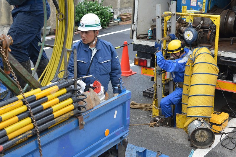 穴が開いた送電線のある地中に降りるため、マンホール(右)内に入る作業員=大阪府吹田市で2017年8月23日午後5時6分、小松雄介撮影