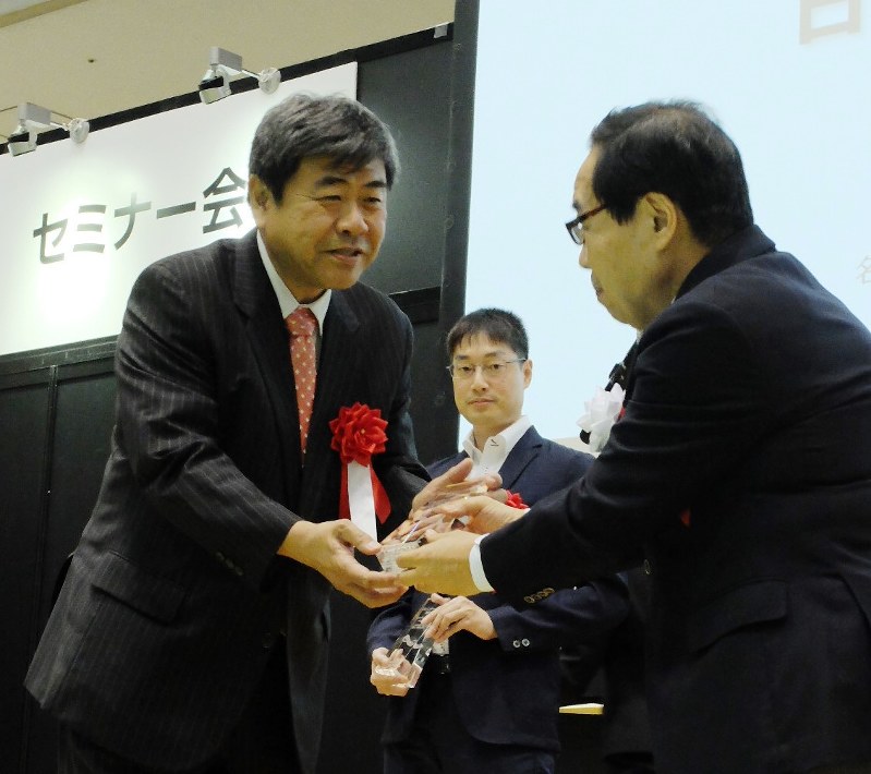表彰式でトロフィーを受け取る春日敏宏・名古屋工業大教授(左)=東京都江東区で