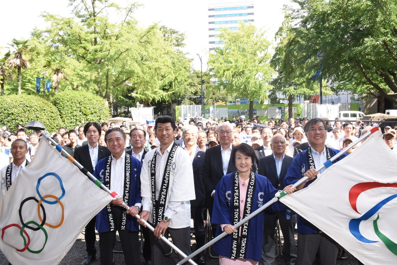 五輪旗とパラリンピック旗を手に笑みを浮かべる黒岩知事(左から3人目)と三浦さん(同5人目)ら=横浜市中区で