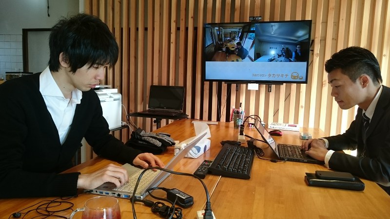 サテライトオフィスで仕事をする「CRANE」社長の安司寛太さん(左)と大井拓哉さん(右)。奥のモニターには東京のオフィスの様子が映し出されている=高崎市で