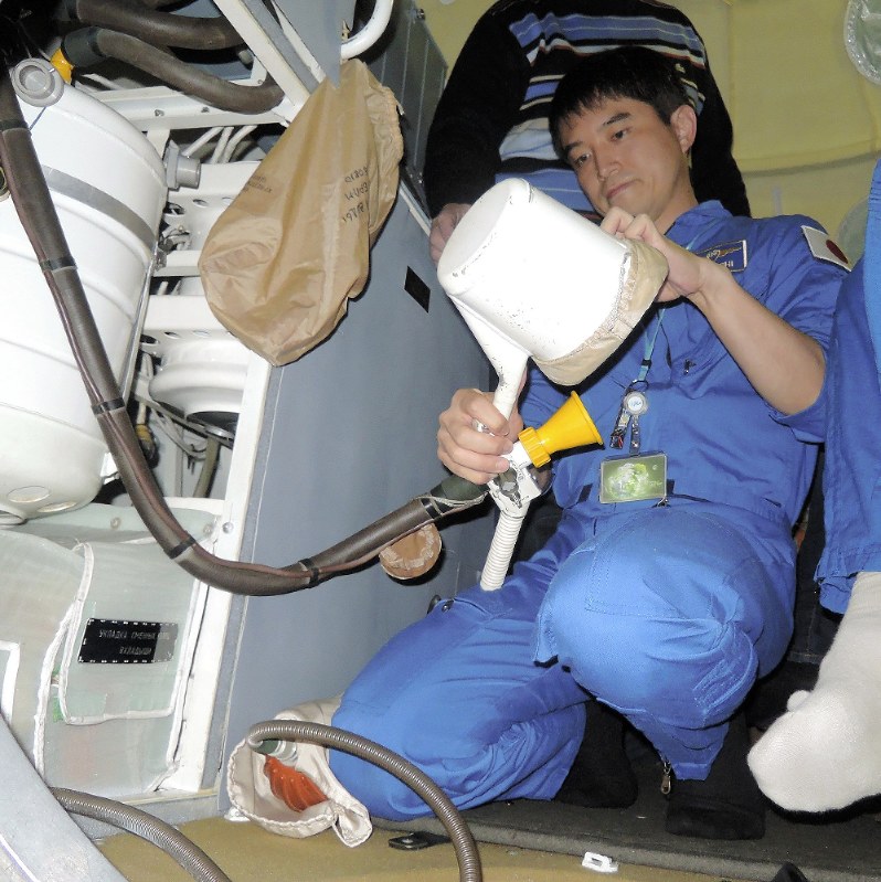 地上で宇宙でのトイレ訓練をする大西卓哉宇宙飛行士。手元の小さなホースでおしっこを吸い取る=JAXA提供