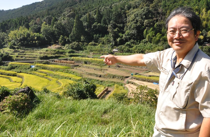 稲刈りが進む棚田を指差す沢畑さん
