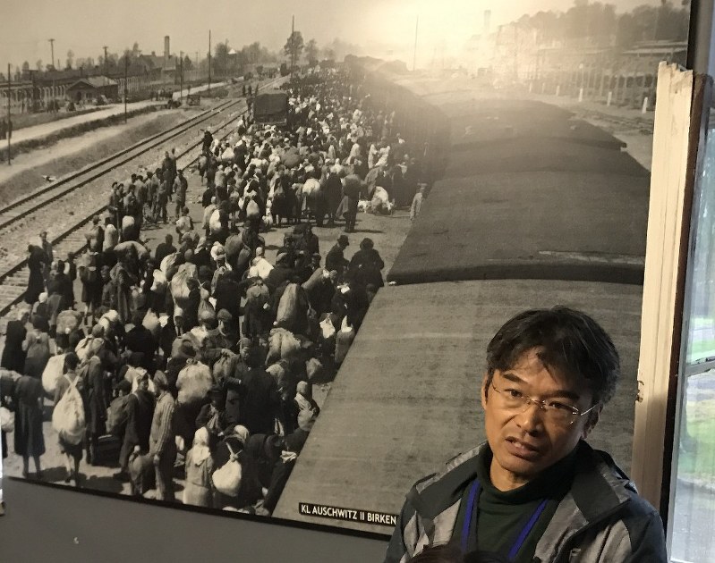 説明する中谷剛さん。写真は、ビルケナウに停車した列車から降り立つ人々。1車両あたり約70人がトランクとともに詰め込まれ、数百キロ以上も離れたところから、運ばれた=ポーランド・オシフィエンチムで2017年9月17日午後3時8分、鈴木美穂撮影