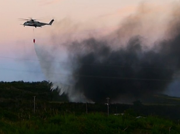 米軍ヘリCH53が着陸後炎上した現場で消火活動に当たる米軍のヘリコプター=沖縄県東村で11日午後(琉球新報提供)