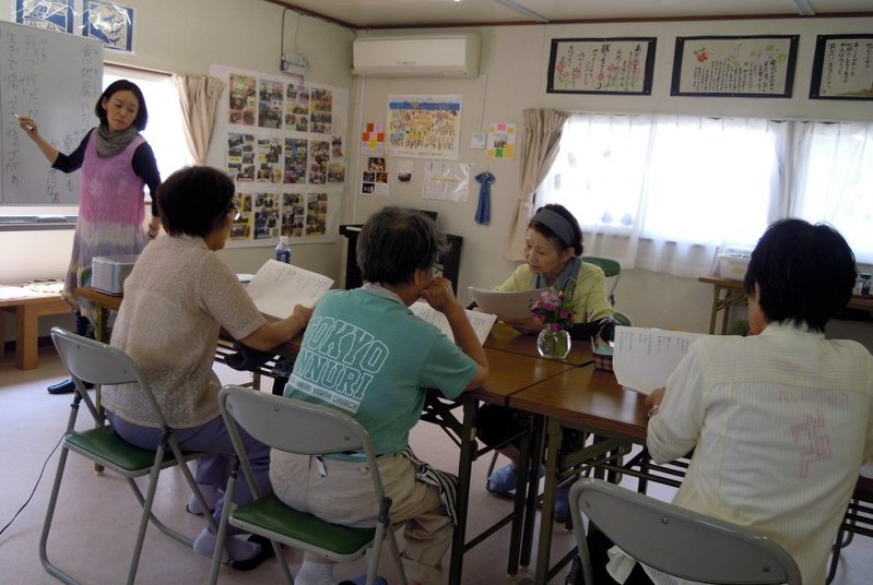 大船渡市の仮設住宅集会所で、啄木の短歌を土地の言葉に訳す新井さん(左)と参加者のおんばたち=2015年8月6日(新井さん提供)