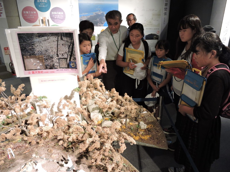子供たちにジオラマで沖ノ島の古代祭祀を説明する鎌田さん(左から3人目)