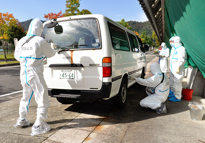 滋賀県高島市での2016年の訓練で、住民の避難に使われた車の放射線量を測定し、拭き取り除染をする関西電力の社員=同市今津町で、塚原和俊撮影