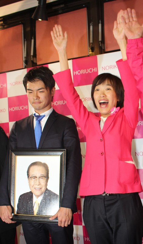 義父の故堀内光雄元通産相の遺影のそばで万歳する堀内詔子氏=富士吉田市中曽根1の事務所で22日午後11時23分