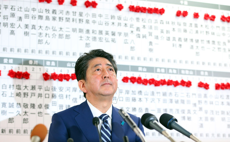 赤い花に囲まれて、硬い表情でテレビの中継に臨む安倍晋三首相=東京都千代田区で22日午後10時40分、小川昌宏撮影