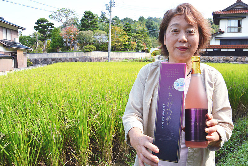 古代米の水田を背に、新たに発売した日本酒「比賣神乃雫」を手にする庄倉三保子代表=鳥取県南部町清水川で、小野まなみ撮影