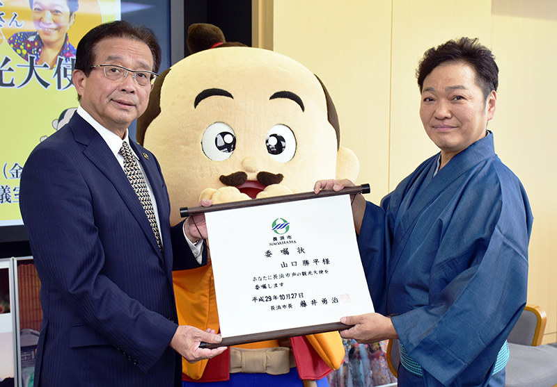 滋賀県長浜市の藤井勇治市長(左)から「長浜市PR大使」の委嘱状を受け取る山口勝平さん。中央は「ひでよしくん」=同市役所で、若本和夫撮影