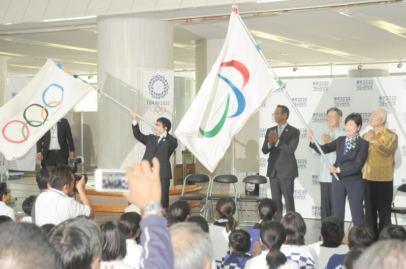 東京五輪・パラリンピックのフラッグツアー歓迎イベントで五輪旗を振る糸数陽一選手(左端)とパラリンピック旗を振る小池百合子都知事(右から2人目)=那覇市の沖縄県庁で