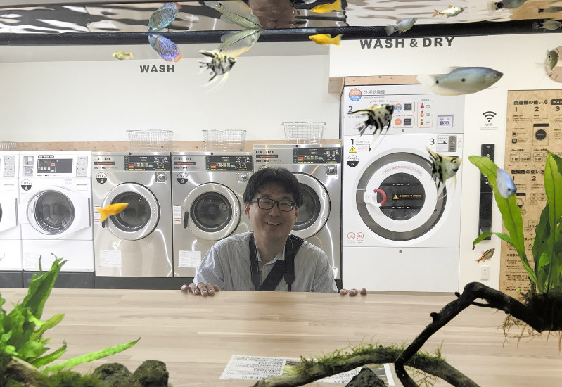 水槽ごしに笑顔を見せる=東京都江戸川区の「AQUARIUM LAUNDRY」で
