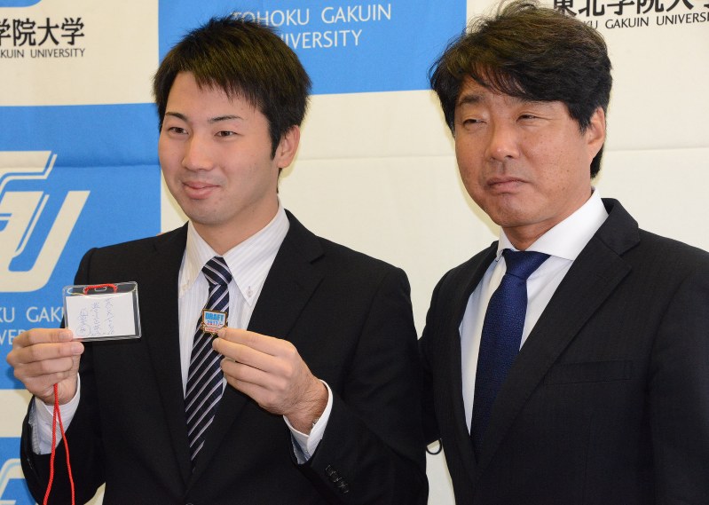 栗山英樹監督のメッセージが書かれた入館証を掲げる鈴木遼太郎投手(左)と西俊児スカウト=仙台市泉区の東北学院大で
