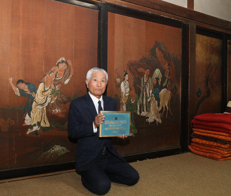 登録プレートを持ち、仙人が描かれた杉戸の前に座る滑川藤彌さん=銚子市野尻町の滑川家で