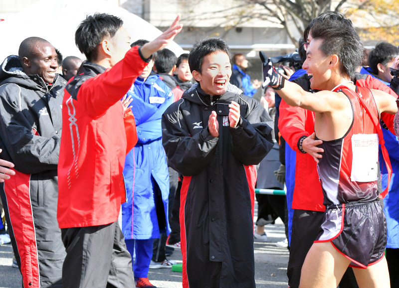 1位でフィニッシュしたアンカーの定方選手(右端)を笑顔で迎えるMHPSのチームメートら=森園道子撮影