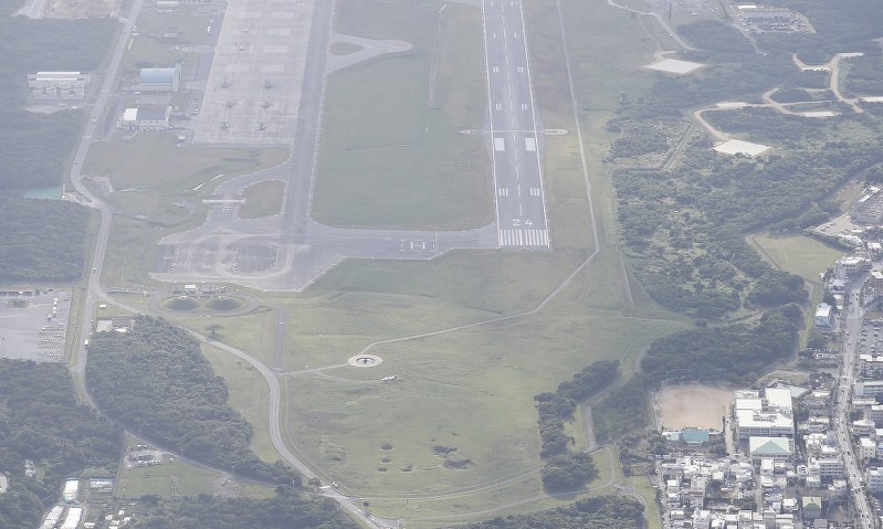 沖縄県宜野湾市の市立普天間第二小学校(手前右)と米軍普天間飛行場。部品が落下したとみられる機体が駐機されている=沖縄県宜野湾市で13日午後、本社機「希望」から