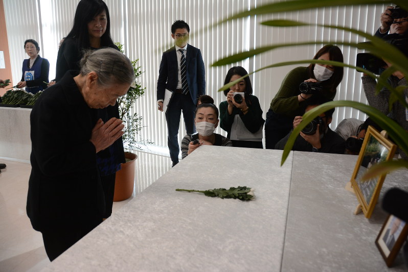 みきおさん一家の写真に手を合わせる母節子さん=世田谷区で