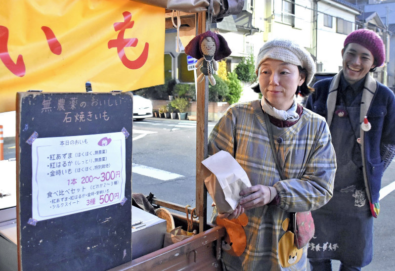 客に焼き芋を渡す村田さん(左)と斉藤さん=埼玉県戸田市で