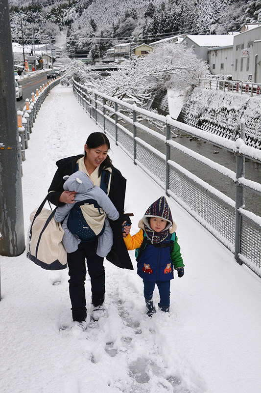 「こんなに積もるなんてびっくり」と雪道を注意しながら歩く木村さん親子=愛媛県伊予市中山町中山で、松倉展人撮影
