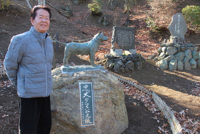 ふるさとの方を見守っているという忠犬タマ公の像と石碑に足を運ぶ衣笠観光協会の鈴木会長=横須賀市で