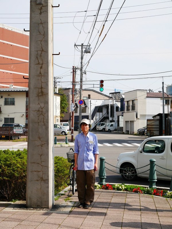 歴史ある日本最古のコンクリート電柱と写真に収まる須賀亮行さん=北海道函館市で2016年9月(須賀さん提供)