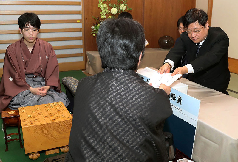 久保利明王将から封じ手を受け取る立会の小林健二九段(右)。左は挑戦者の豊島将之八段=佐賀県上峰町の「大幸園」で2018年1月27日午後6時9分