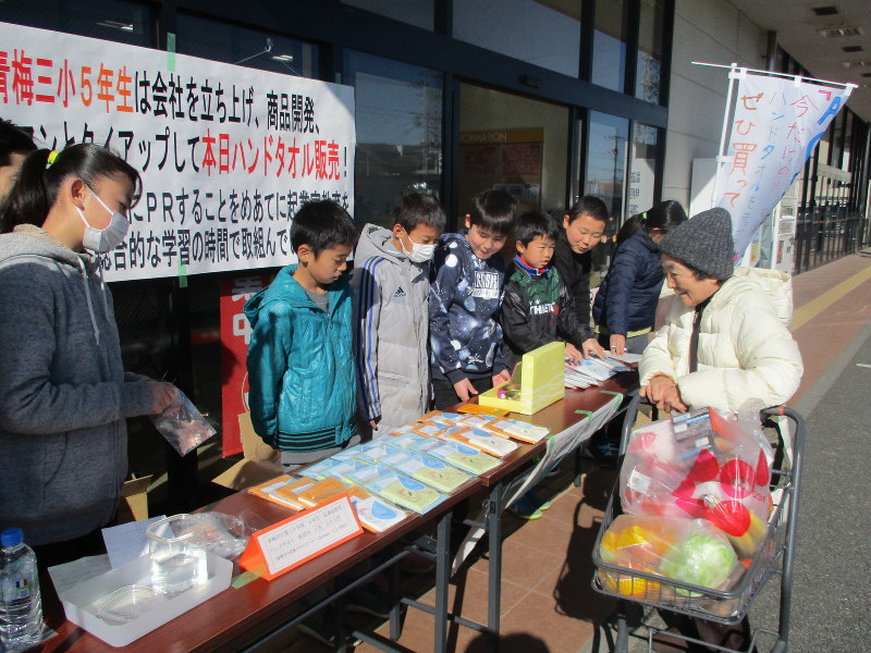 青梅市内のスーパー店頭で皆でデザインを決めたハンドタオルを販売する児童ら=青梅市内で