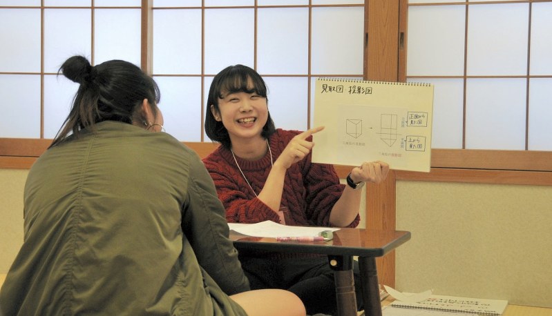 指導役の大学生(右)は数学の見取り図や投影図を生徒に分かりやすく理解してもらうため、スケッチブックに手書きした教材で説明をする=東京都で