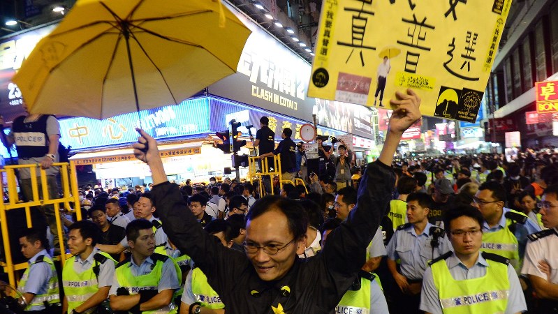 「真の普通選挙を」と書いたボードを持ち警官隊の前に立つ男性=香港で2014年11月26日、隅俊之撮影