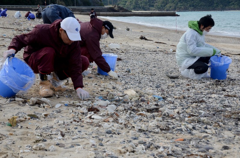 石に付着したり砂混じりになっている漂着油を回収する県職員ら=鹿児島県奄美市名瀬の朝仁海岸で2018年2月8日、神田和明撮影