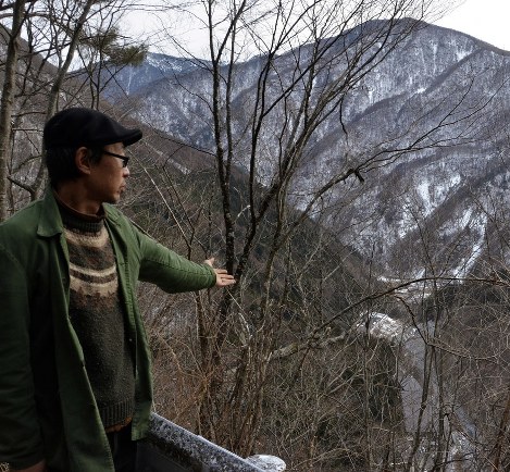 自宅近くの高台から谷あいで進むリニアの工事現場を示す谷口さん＝長野県大鹿村で、森健太郎撮影