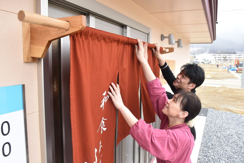 空き地の目立つ中心市街地で、和食屋「味彩」ののれんをかける阿部昌浩さんと裕美さん=岩手県陸前高田市高田町で、2018年2月、後藤結有撮影