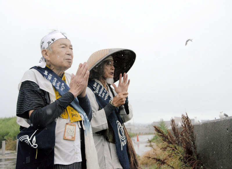犠牲者の鎮魂のため、同行者とともに海に向かって般若心経を唱える増田哲将さん(左)=青森県八戸市の蕪島神社前で