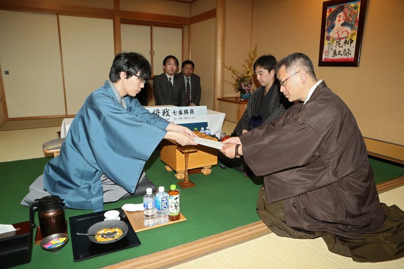 立会人の中村修九段(右手前)に封じ手を手渡す挑戦者の豊島将之八段(左)。右奥は久保利明王将=長野県松本市の松本ホテル花月で2018年3月14日午後