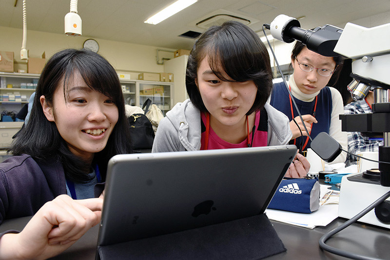 顕微鏡で見える微生物をタブレット端末に映して眺める指導役の奈良女子大生(左)と参加者たち=奈良市で、郡悠介撮影