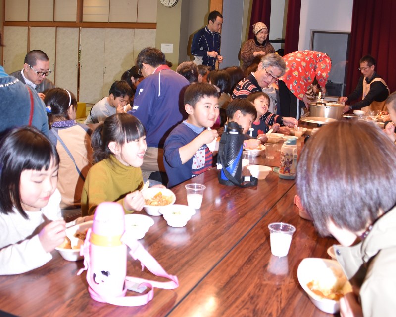 昼食会で一緒にカレーを食べる子供や保護者、ボランティアら
