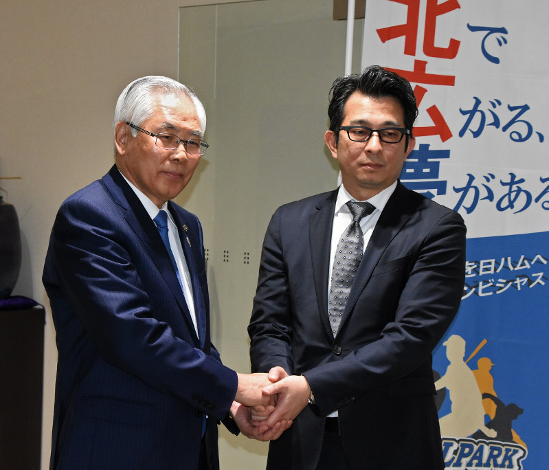握手する上野正三市長(左)と日本ハム球団の前沢賢・事業統轄本部長=北広島市役所で
