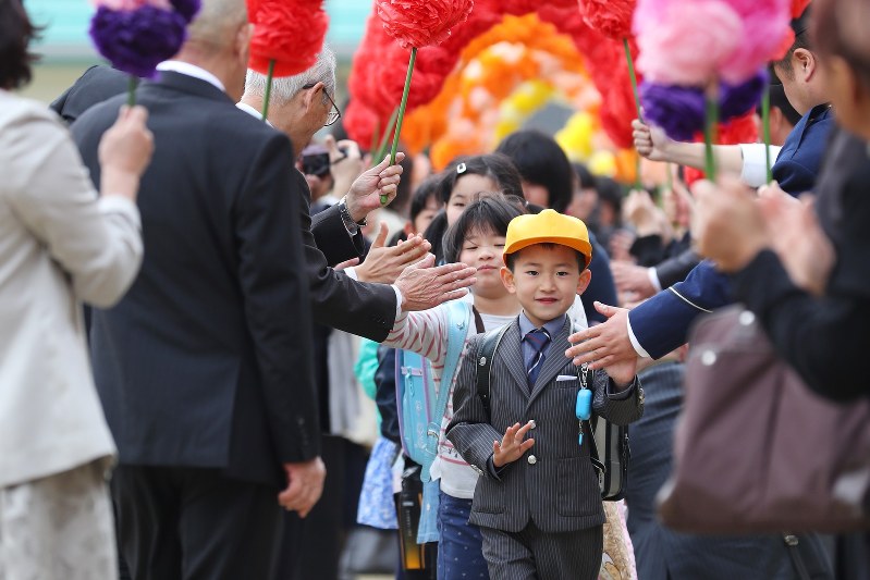 開校式前に村民手作りの「花のトンネル」で出迎えられる葛尾村立小・中学校の児童生徒たち=福島県葛尾村で2018年4月6日午前、喜屋武真之介撮影