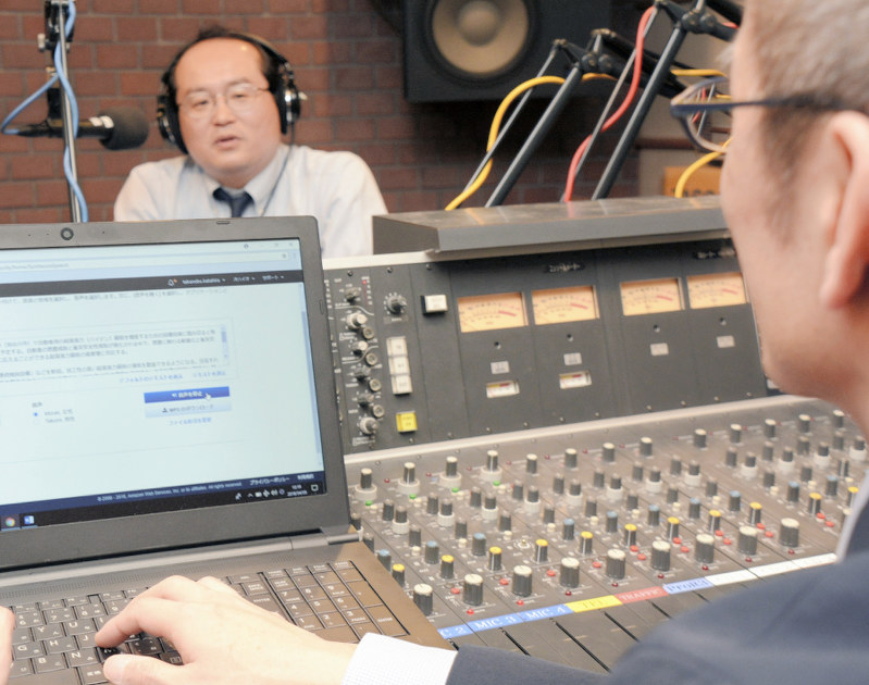 パソコンでAIの音声を編集しながら番組収録をする片平享伸さん(手前)と、番組で解説役を務める山本学さん=神戸市中央区のエフエム兵庫で
